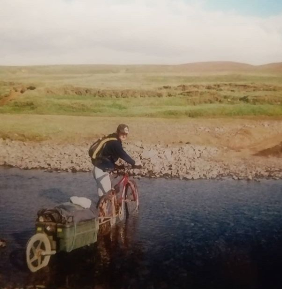 A cyclist crosses an Icelandic river with a cycle trailer