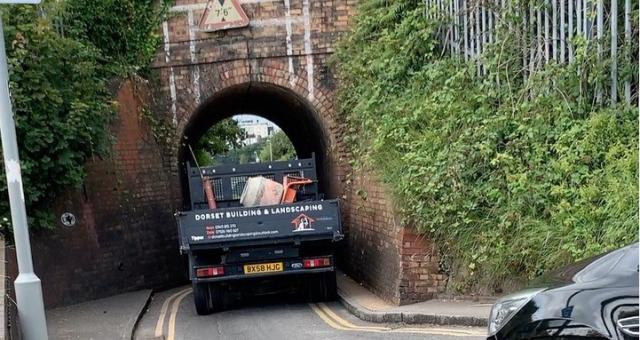 A large vehicle driving through the very narrow Keyhole Bridge underpass, nearly unable to fit through