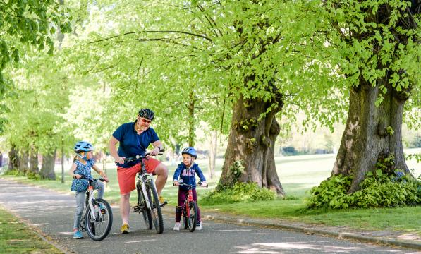 A father and two children cycling in a pleasant green space 