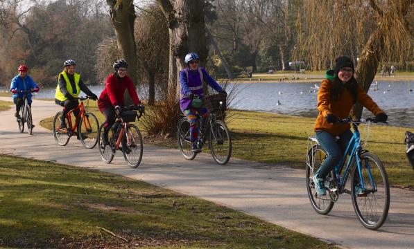 Several people in normal clothes, cycling along a path next to a river