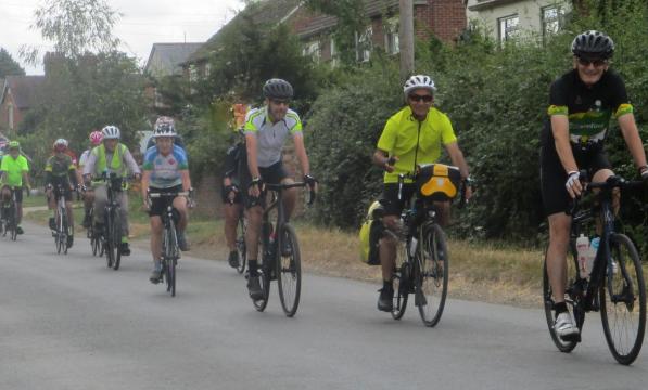 Picture showing a group of male and female cyclists cycling on a quiet road. 