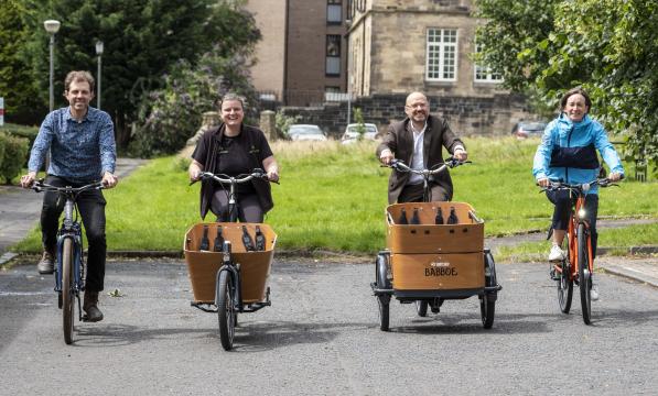 Active Travel Minister Patrick Harvie is riding a cargo bike, beside Suzanne Forup of Cycling UK who is riding a standard bike and representative from Bike for Good in Glasgow. The is a green space behind them